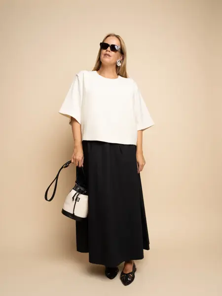 Damemodell med sorte solbriller, hvit topp, sort skjørt og sort og hvit veske og sorte flate sko.