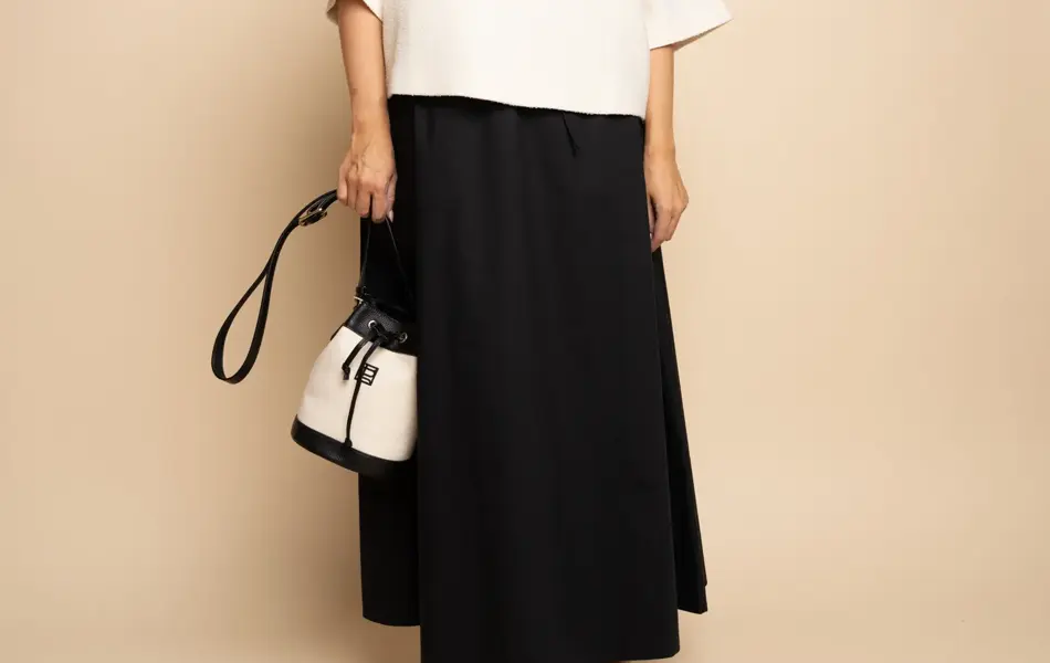 Damemodell med sorte solbriller, hvit topp, sort skjørt og sort og hvit veske og sorte flate sko.