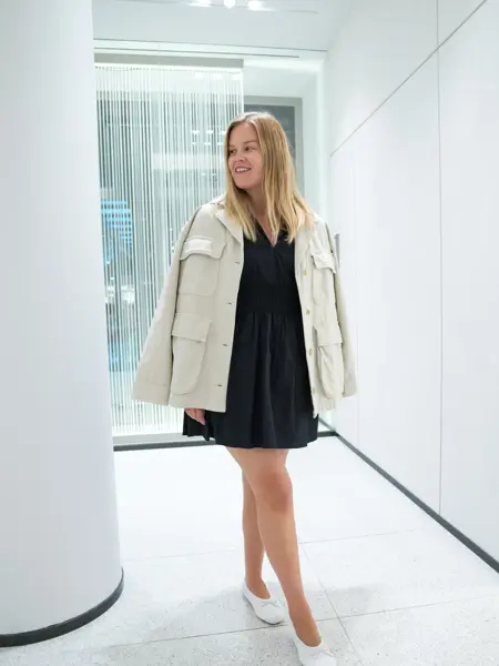 Jente med blondt hår, har på seg en knelang sort kjole med hvot dressjakke over 