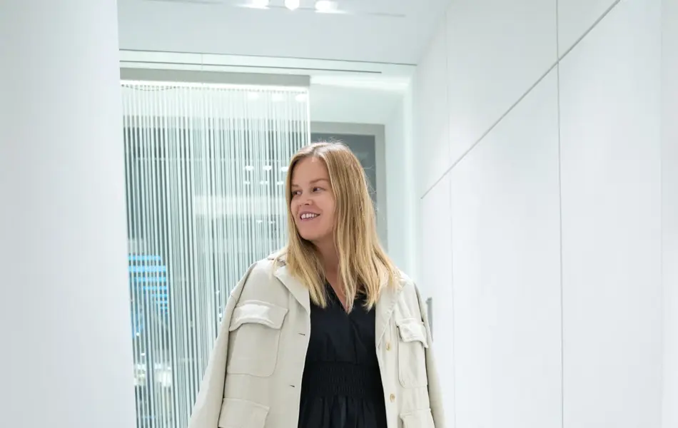 Jente med blondt hår, har på seg en knelang sort kjole med hvot dressjakke over 