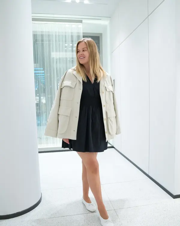 Jente med blondt hår, har på seg en knelang sort kjole med hvot dressjakke over 