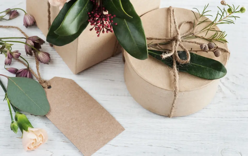 Hand crafted gifts and tag on white wooden background, with floral decoration