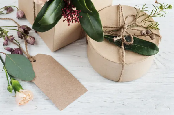 Hand crafted gifts and tag on white wooden background, with floral decoration