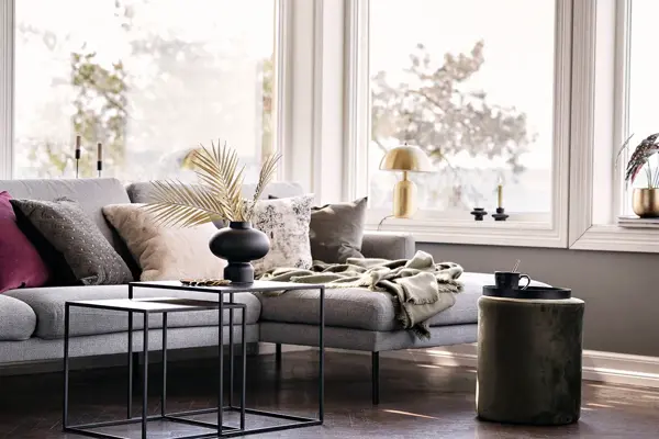 Sofa med puter og sort vase med strå