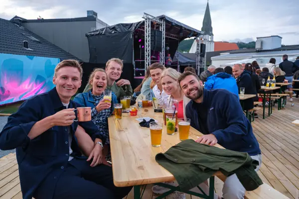 Fire menn og to damer nyter drinker rundt et bord på utekonsert