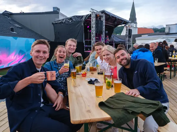 Fire menn og to damer nyter drinker rundt et bord på utekonsert