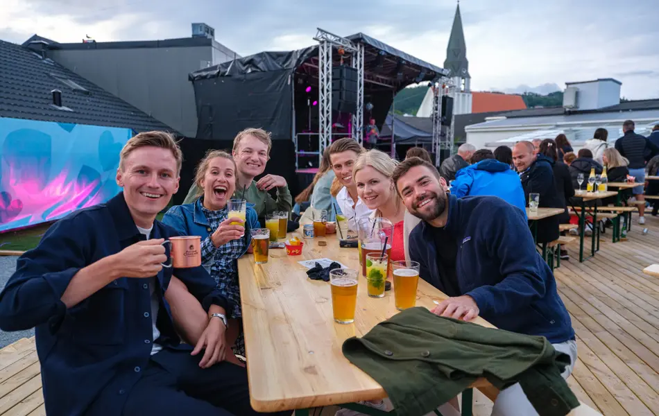 Fire menn og to damer nyter drinker rundt et bord på utekonsert