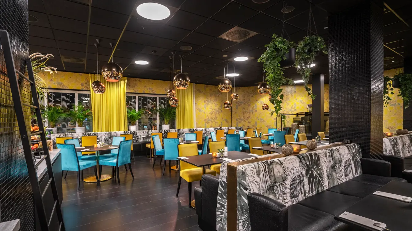 Frokostsal, gul tapet, runde bord, blå og gule stoler.