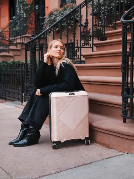 Jente sitter på trapp i en storby med en rosa koffert ved siden av seg.