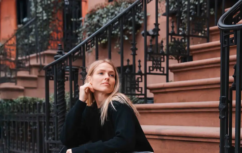 Jente sitter på trapp i en storby med en rosa koffert ved siden av seg.