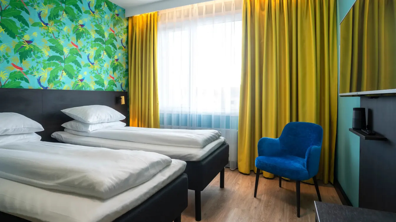 Gule gardiner, tapetvegg, to enkeltsenger, parkettgulv, blå stol, TV, vindu