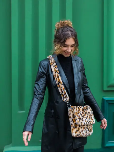En dame med svart skinnjakke og fluffy veske i leopardmønster står foran en grønn vegg
