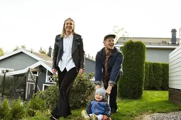 Par med litebarn i en hage med grønt gress og hus i bakgrunnen