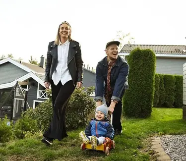 Par med litebarn i en hage med grønt gress og hus i bakgrunnen