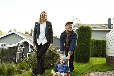 Par med litebarn i en hage med grønt gress og hus i bakgrunnen