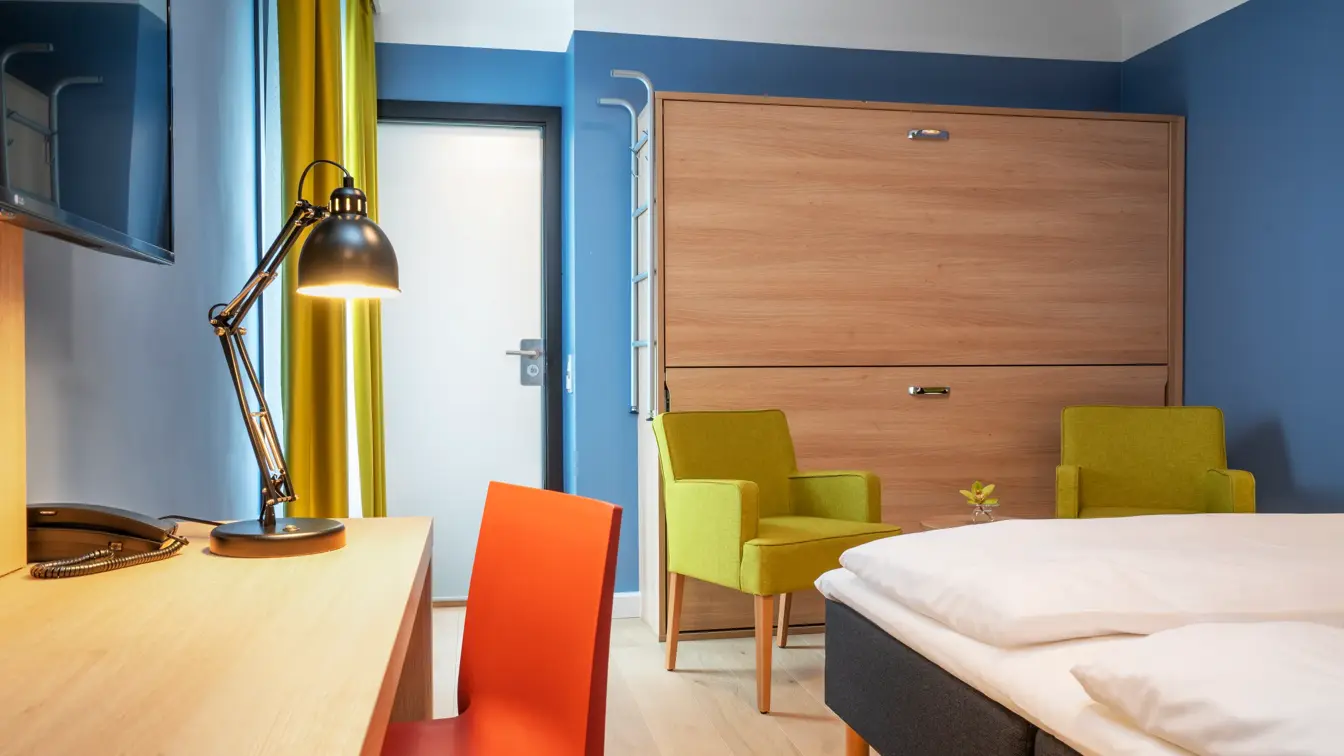 Skrivebord, TV, skap køyeseng, to gule stoler med lite bord og dobbeltseng på familierom på Thon Hotel Astoria
