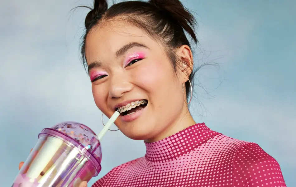 Portrett av glad tenåringsjente med vannflaske stående mot farget bakgrunn