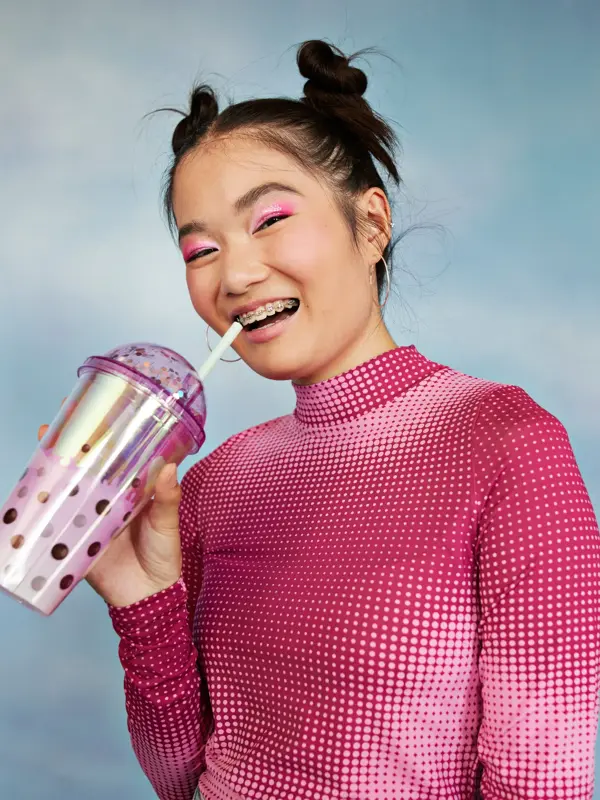 Portrett av glad tenåringsjente med vannflaske stående mot farget bakgrunn