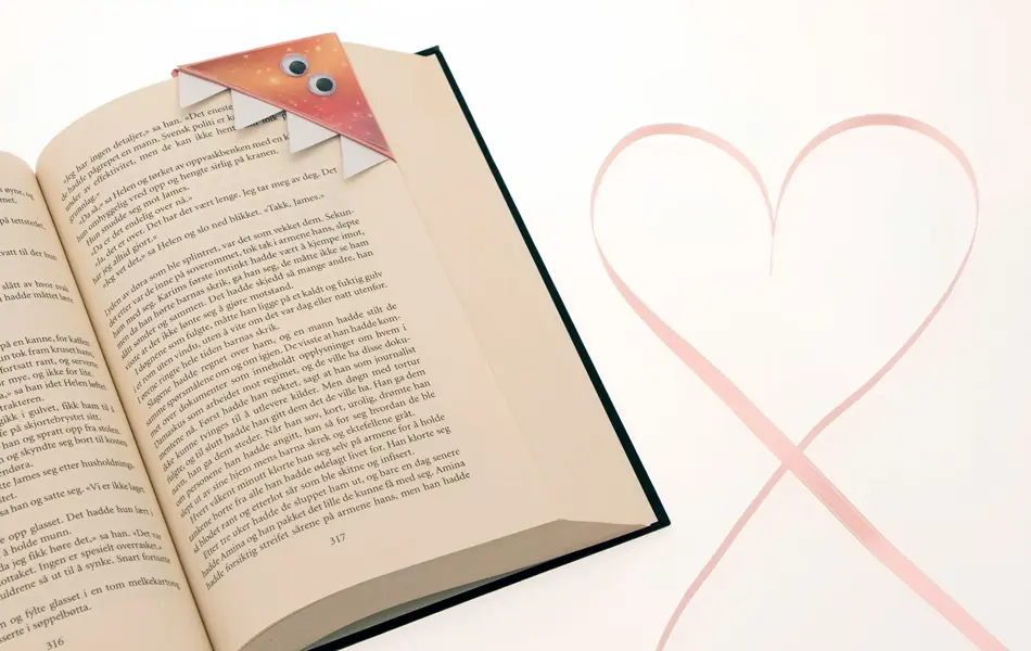 Bok med hjemmelaget "monster"bokmerke og et hjerte ved siden