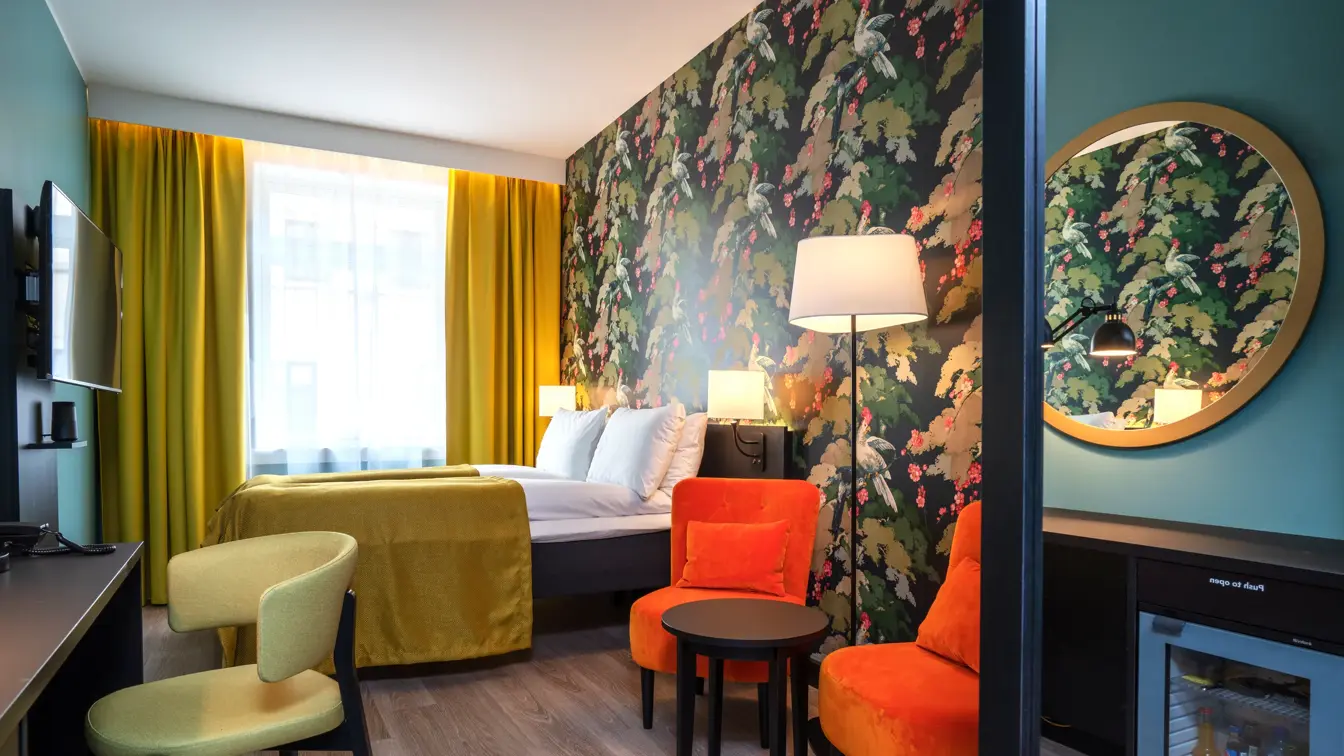 Skrivebord med gul stol og TV, separate senger med gult sengeteppe, gule gardiner, fargerikt tapet og oransje stoler i twin rom på Thon Hotel Bristol Bergen