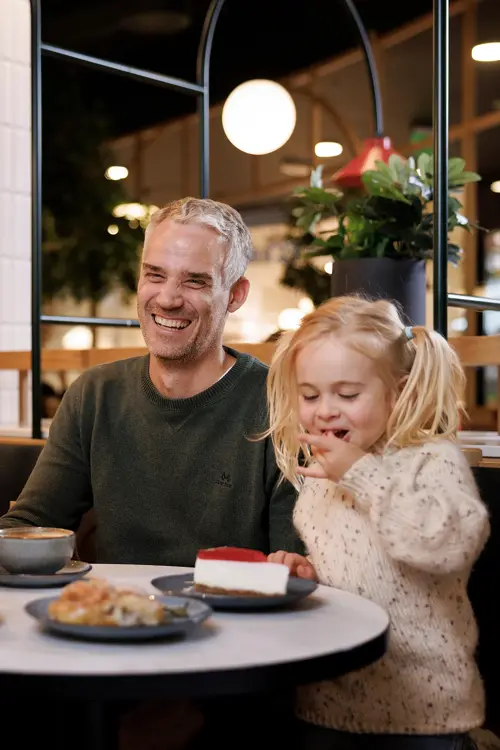En mann, en kvinne og et barn sitter ved et bord på en kafé, mannen og kvinnen smiler til hverandre