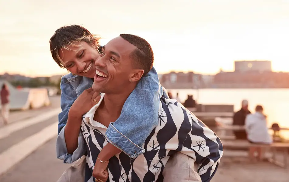 En ung smilende mann med en ung smilende kvinne på ryggen