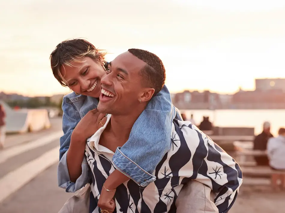 En ung smilende mann med en ung smilende kvinne på ryggen