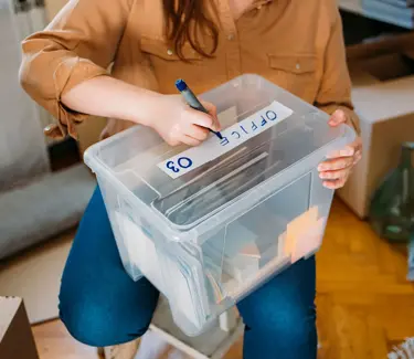 En dame lager merkelapp på en kasse med ting som skal settes bort