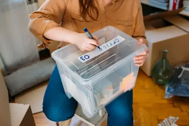 En dame lager merkelapp på en kasse med ting som skal settes bort
