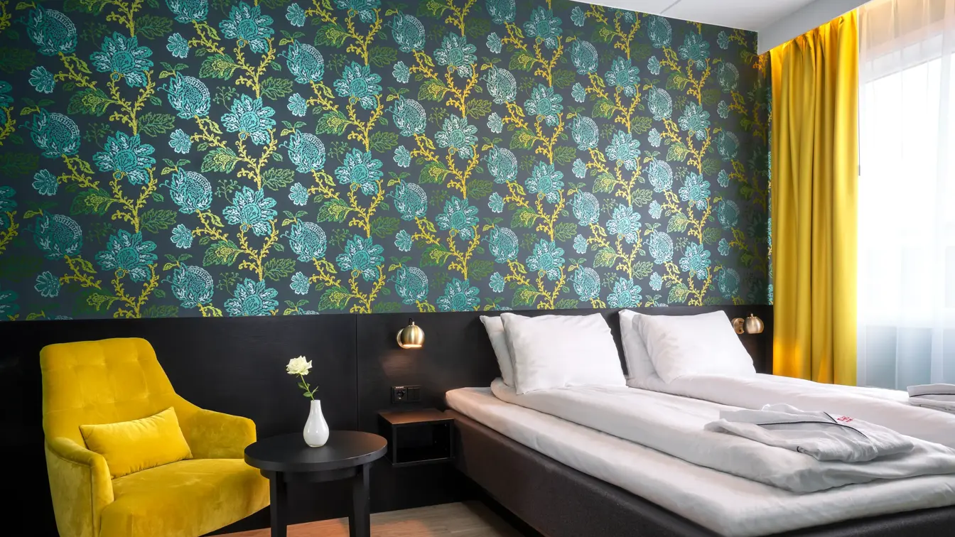 Grønn og turkis mønstrete tapet med blomster, gul stol med rundt bord og dobbeltseng i suite på Thon Hotel Kirkenes