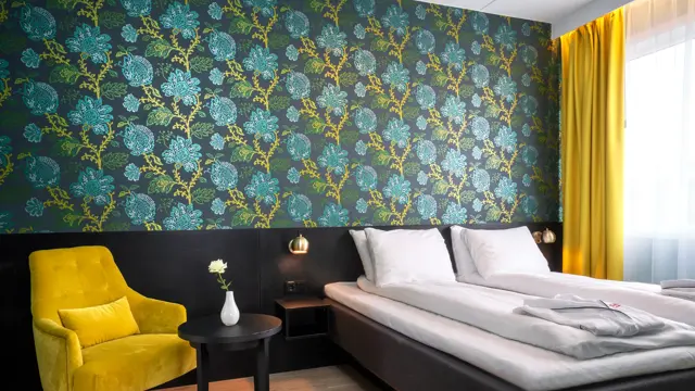 Grønn og turkis mønstrete tapet med blomster, gul stol med rundt bord og dobbeltseng i suite på Thon Hotel Kirkenes