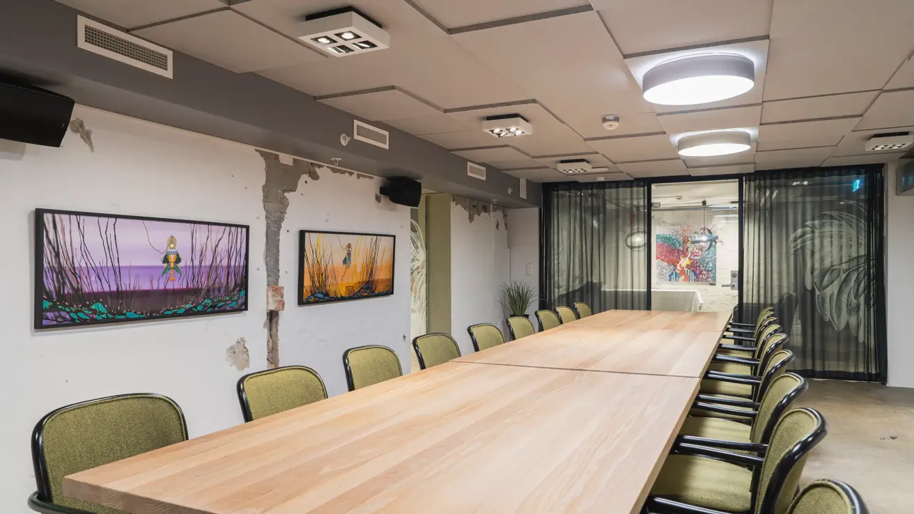 Møterom i rustikk stil, langbord med stoler rundt, og fargerike bilder på veggene