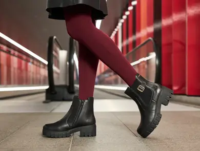 Nærbilde av et par ben i rød strømpebukse og boots foran en rulletrapp.