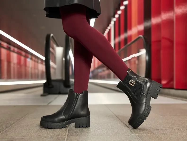 Nærbilde av et par ben i rød strømpebukse og boots foran en rulletrapp.