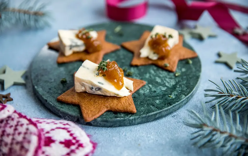 Stjerneformede pepperkaker på et fat med blåmuggost og syltetøy på toppen