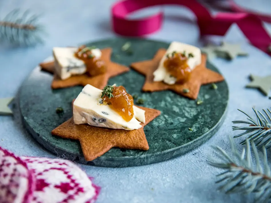 Stjerneformede pepperkaker på et fat med blåmuggost og syltetøy på toppen
