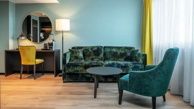 Stue, sofa, salongbord, grønn lenestol, gule gardiner, vindu, TV, parkettgulv, skrivebord, speil på veggen, gul skrivebordstol, gulvlampe 