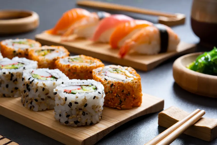 Sushi set uramaki and spicy sushi rolls served on bamboo tray. Various kinds of sushi pieces served on black slate with wooden chopstick. Japanese traditional food with bamboo service.