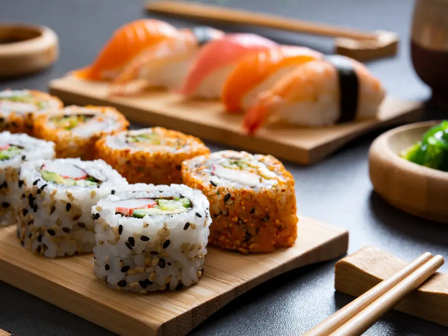 Sushi set uramaki and spicy sushi rolls served on bamboo tray. Various kinds of sushi pieces served on black slate with wooden chopstick. Japanese traditional food with bamboo service.