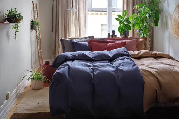 Soverom med oppredd dobbeltseng, teppe på gulvet, vindu med gardiner og grønne planter