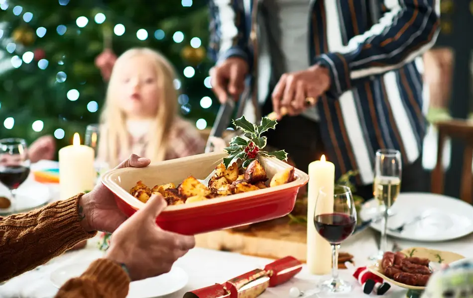 person som tar i mot ildfastform med poteter over middagsbordet