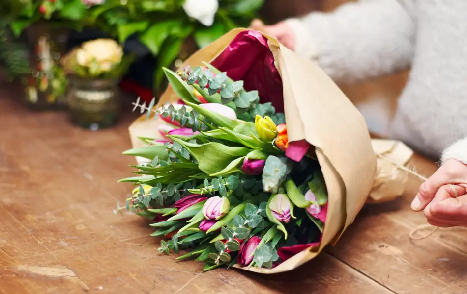 Cropped shot of a pretty floral bouquet being completed on a wooden counter top