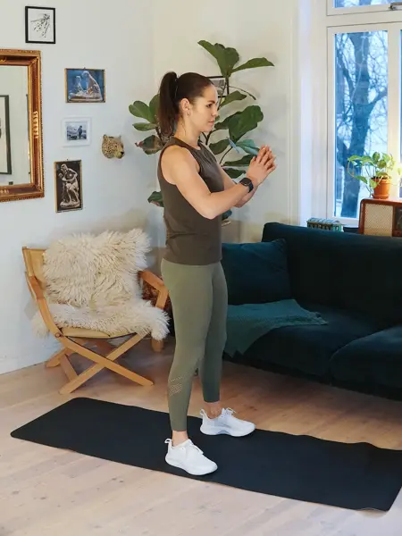 treningsekspert Anna Johansen trener på matte på gulvet, mørkegrønn sofa i bakgrunnen, lys stol med pels oppi, str grønn plante, bilder på veggen