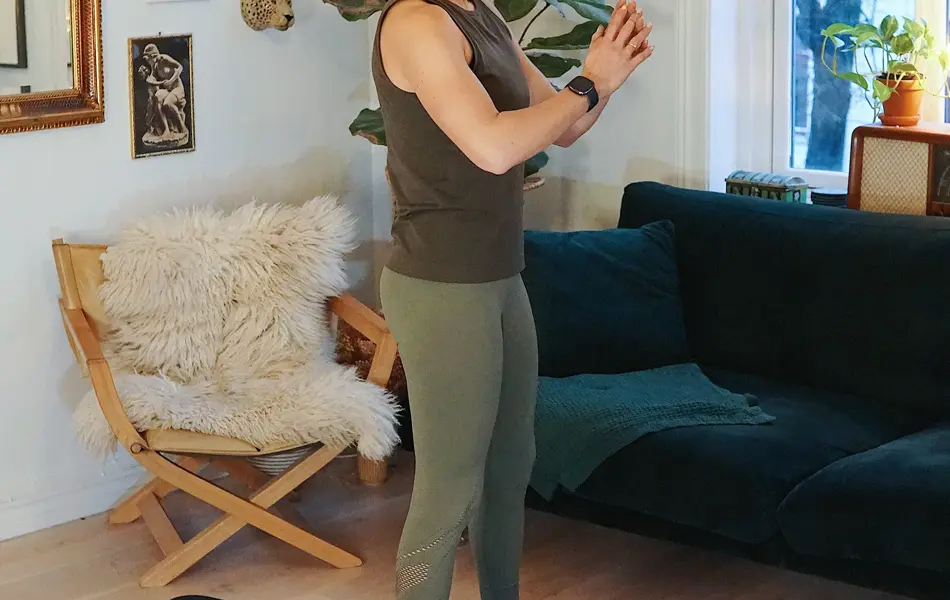 treningsekspert Anna Johansen trener på matte på gulvet, mørkegrønn sofa i bakgrunnen, lys stol med pels oppi, str grønn plante, bilder på veggen