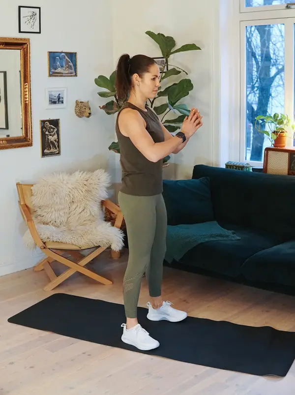 treningsekspert Anna Johansen trener på matte på gulvet, mørkegrønn sofa i bakgrunnen, lys stol med pels oppi, str grønn plante, bilder på veggen
