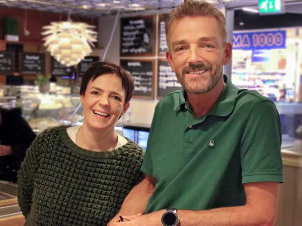Dame og mann smiler til kamera med Rema 1000 i bakgrunnen