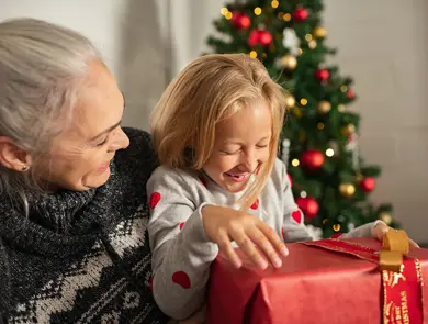 datter på mors fang foran juletre, med julegave i hendene