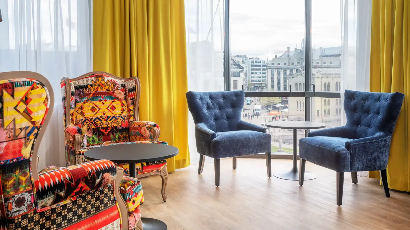 Stoler med fargerikt mønster, blå stoler, sorte runde bord, gule gardiner og store vinduer med utsikt i lounge på Thon Hotel Cecil