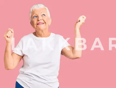 En eldre kvinne som står og danser mot en rosa bakgrunn.