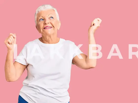 En eldre kvinne som står og danser mot en rosa bakgrunn.